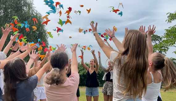 Schülerinnen werfen Vögel aus Papier nach oben